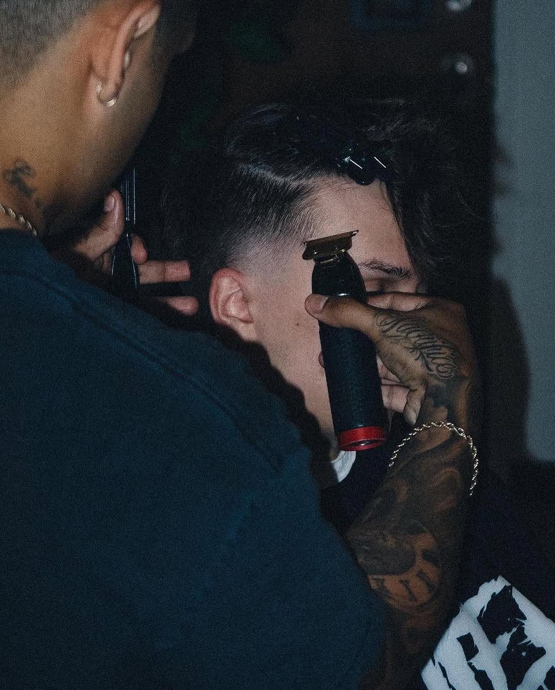 Mid-cut clippers in tattooed hand at the chair.
